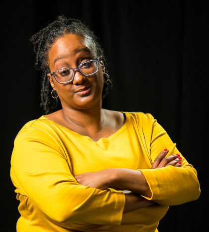 
		Kayla Hamilton headshot. 
		Kayla is a Black woman with shoulder length locs, half-tied up. She regards the camera with a knowing smile, with arms crossed. She wears glasses, small hoop earrings, and a warm yellow 3/4 shirt. Photo by Cherylynn Tsushima.		
		